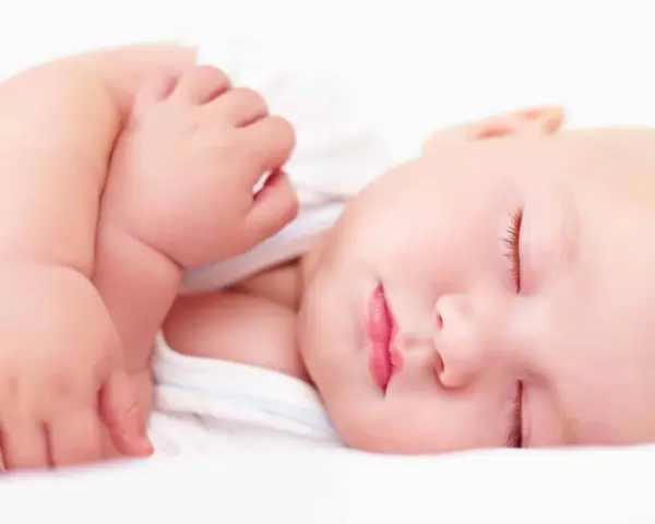 Ein friedlich schlafendes Baby, etwa 4 Monate alt, mit geschlossenen Augen und leicht geöffneten Lippen. Die zarte Haut und die kleinen Händchen sind gut zu erkennen.