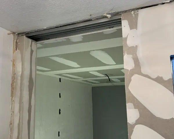 Ouverture dans un mur en cours de travaux de rénovation, avec plaques de plâtre et rails apparents.