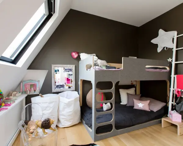 Accogliente camera da letto e cameretta insieme, con letto a castello grigio, giocattoli, cuscini a forma di stella e sacchi bianchi.