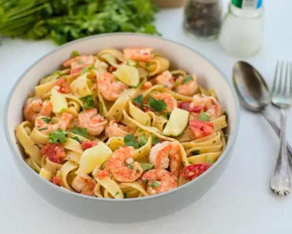 Pyszne tagliatelle z krewetkami, pomidorami i limonką, posypane świeżą natką pietruszki. Idealne danie na szybki obiad.