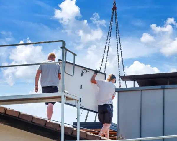Dwaj pracownicy montują panel fotowoltaiczny na dachu. Ciężka praca i ryzyko wypadku to negatywne skutki fotowoltaiki, które często się pomija.