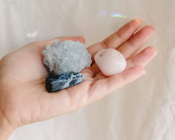 Mano sosteniendo tres piedras: una azul con vetas blancas, una azul pálido cristalina y una rosa pálido pulida. Son piedras para embarazadas.