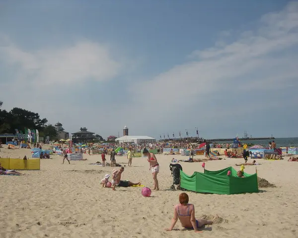 Słoneczna plaża w Darłowie tętni życiem. Ludzie opalają się, bawią z dziećmi i odpoczywają pod kolorowymi parawanami.