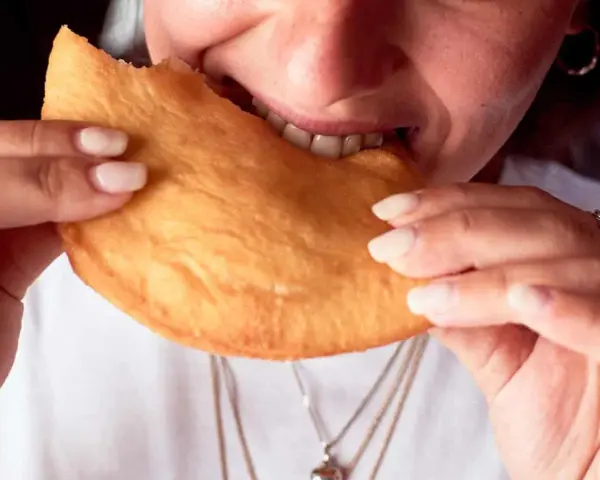 Close-up of a person biting into a golden-brown, fried pastry.