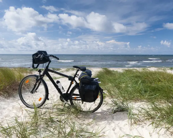 Rower z sakwami na plaży, gotowy do podróży trasą rowerową R10. Morze i niebo w tle.