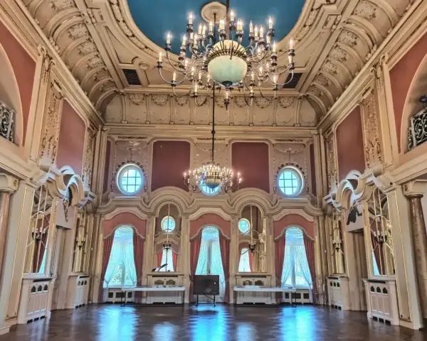 Wnętrze pałacu w Poznaniu, idealne do zwiedzania. Bogato zdobiony sufit, kryształowe żyrandole i eleganckie zasłony tworzą atmosferę dawnej świetności.
