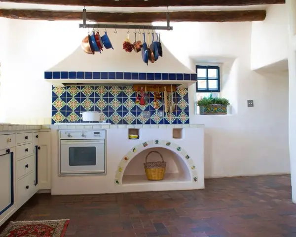 Cocina rústica con azulejos coloridos y detalles DIY, ideal para decorar casa de campo con poco dinero. Cestas y ollas cuelgan, creando un ambiente acogedor.
