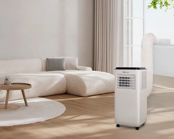 Un aire acondicionado portátil con tubo de escape conectado a la ventana, parte de unas modernas instalaciones hvac, en un salón con sofá beige.