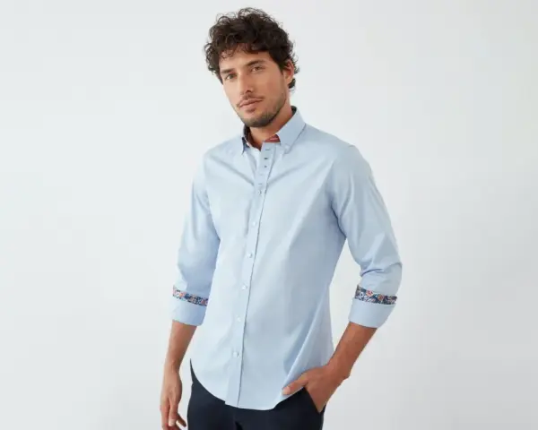 Uomo con camicia blu chiaro, dettagli floreali sui polsini e colletto. Un abbinamento elegante e moderno.