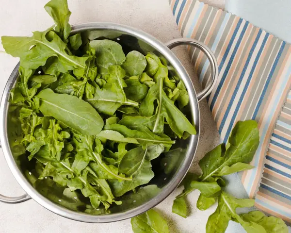 Rukola w durszlaku, idealna do przygotowania jadłospisu tygodniowego dieta FODMAP. Świeże liście na tle kolorowych tkanin.