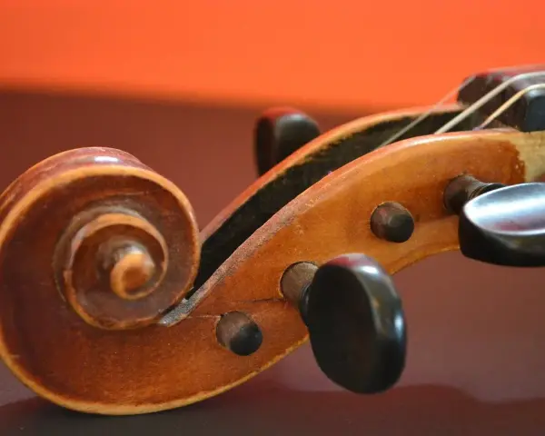 Drewniana ślimacznica skrzypiec, przypominająca spiralę, symbolizuje pierwsze instrumenty muzyczne i ich prostotę.