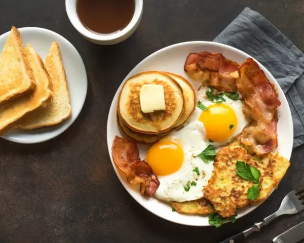 Esempio di colazione proteica per dimagrire: uova, bacon, pancake, toast e succo d'arancia.