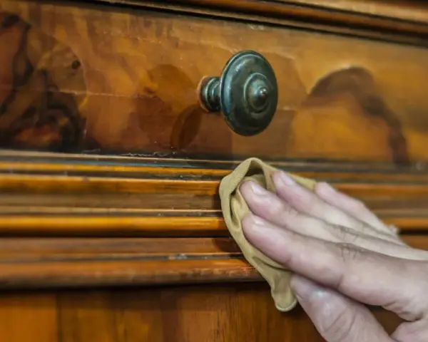 Restauración de mueble antiguo. Mano aplicando betún de judea antes y después, revelando su brillo natural.