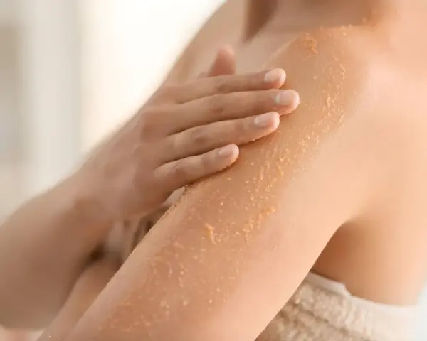 Mano che applica scrub su braccio, rimuovendo la pelle morta dopo la doccia per una pelle liscia e luminosa.