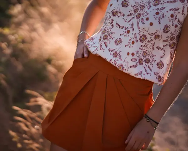 Jupe tulipe orange à plis, portée avec un haut fleuri. Le soleil couchant illumine la scène.