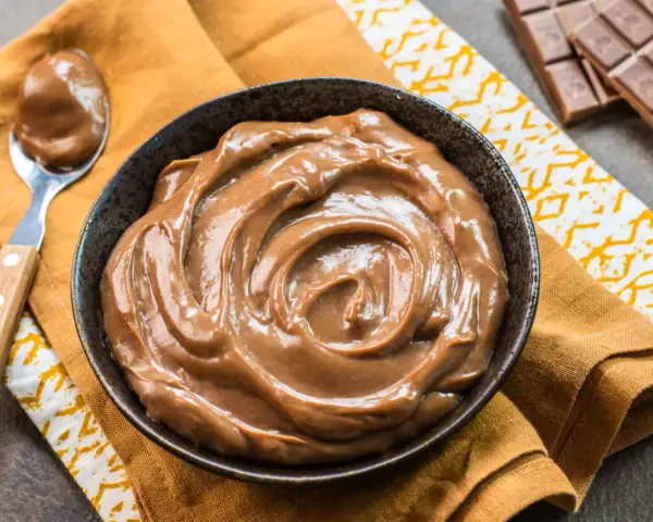 Una ciotola piena di deliziosa crema pasticcera al cioccolato, con una cucchiaiata pronta da gustare. Accanto, una tavoletta di cioccolato.