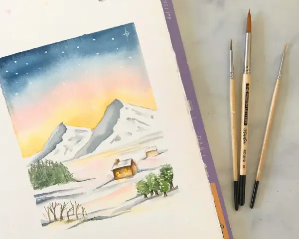 Une aquarelle montagne facile dépeint un paysage hivernal doux avec des montagnes enneigées, des chalets chaleureux et un ciel étoilé. Trois pinceaux sont posés à côté.