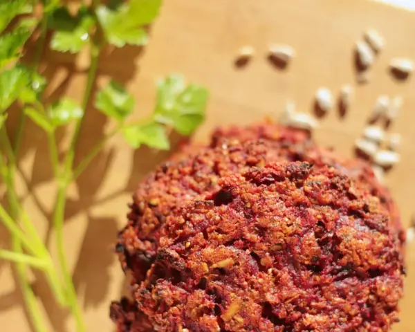 Pyszne kotlety z buraka, przypominające falafel, leżą na desce obok gałązki pietruszki i nasion słonecznika.