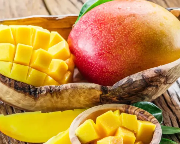 Soczyste, pokrojone w kostkę i w całości mango w drewnianej misce. Owoc ten zawiera mnóstwo witamin.