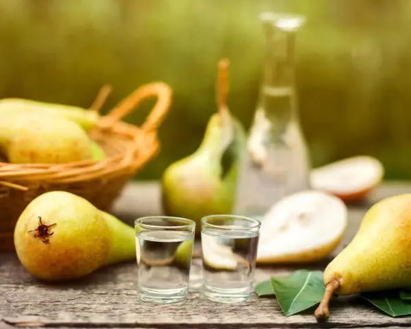 Frische Birnen und zwei Gläschen Schnaps auf Holztisch. Ein Korb voller Birnen im Hintergrund. Perfekt für ein Birnenschnaps Rezept.