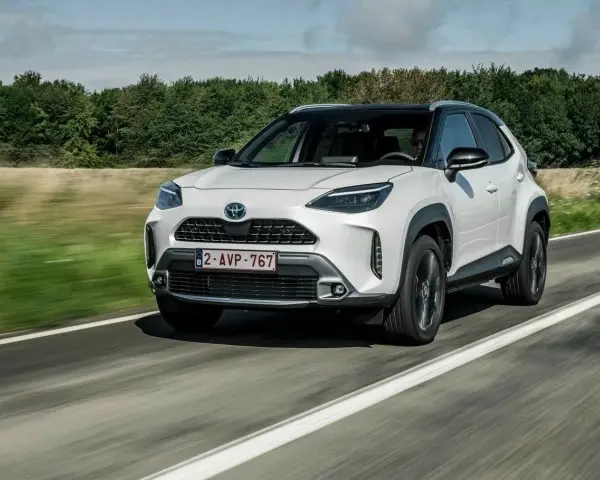 Biały Yaris Cross Hybrid jedzie po drodze, otoczony zielenią.