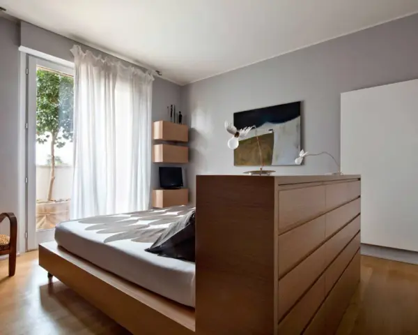 Un moderno **letto in mezzo alla stanza**, con un copriletto a motivi floreali, accanto a una poltrona leopardata e una cassettiera in legno.