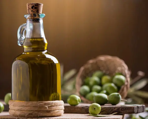 Bottiglia di olio extravergine d'oliva accanto a olive verdi, per capire la differenza tra olio di oliva e olio extravergine.