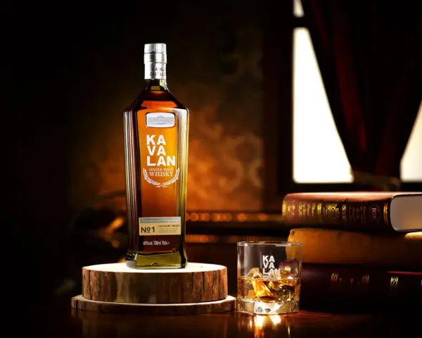 Butelka Kavalan Single Malt Whisky, uznawana za najlepszą polską whisky, obok szklanki z lodem i sterty książek.
