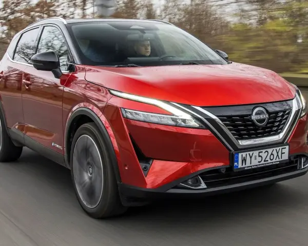Czerwony Nissan Qashqai 2023 z napędem e-POWER jedzie po drodze, za kierownicą siedzi kierowca.