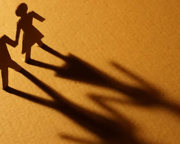 Zwei Papierfiguren, die sich an den Händen halten. Eine Figur scheint sich abzuwenden, während die andere bleibt. Sie sind noch verheiratet und eine neue Beziehung beginnt.