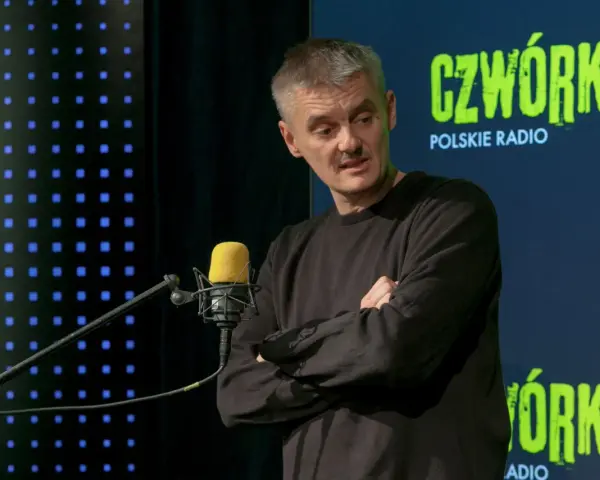 Jacek Sienkiewicz w studiu Polskiego Radia, przed mikrofonem, z rękami skrzyżowanymi na piersi.