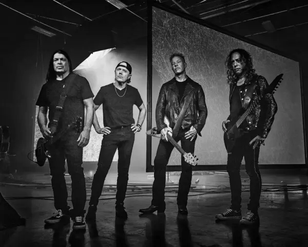 James Hetfield und Metallica im Jahr 2000, bereit für die Bühne. Die Bandmitglieder stehen in dunkler Kleidung, einige mit Gitarren.