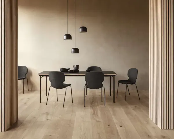 Jadalnia w stylu soft minimalism: czarne krzesła i stół na tle beżowej ściany, oświetlone lampami.