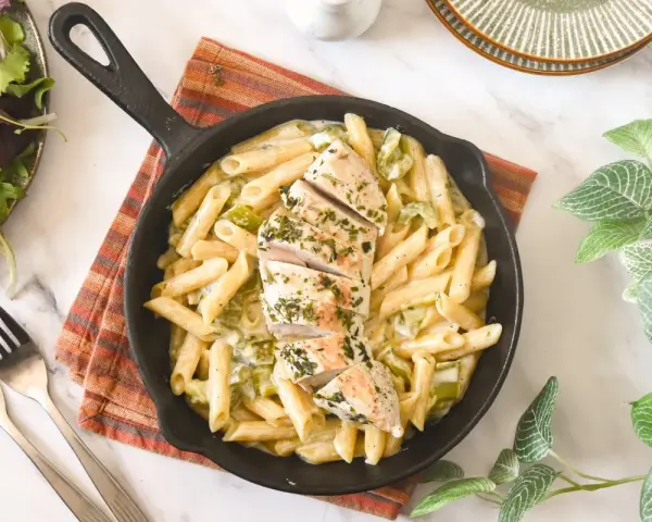 Deliciosa pasta con pollo en sartén, cubierta con hierbas frescas. Acompañada de una ensalada verde y tenedores.
