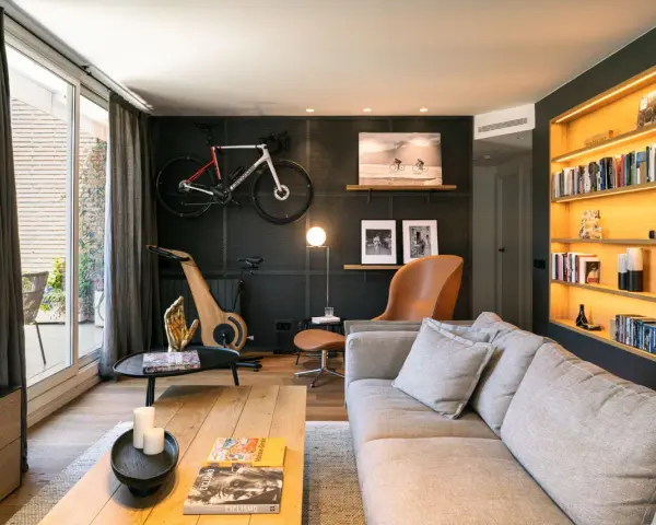 Un salón moderno con bicicleta de carretera colgada, máquina de ciclismo de madera y estanterías iluminadas. Inspiración decoración para deportistas.