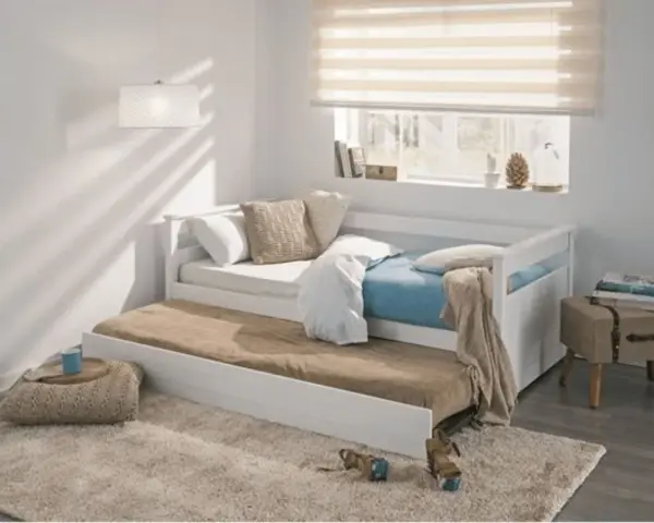 Cama nido blanca con colchones, cojines y manta en un dormitorio juvenil.