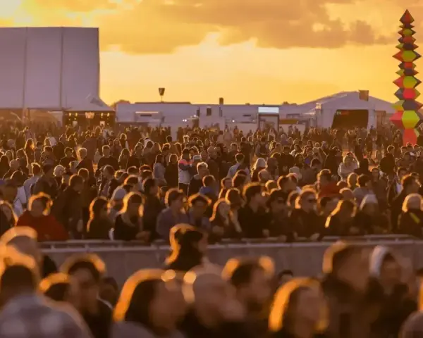 Tłum ludzi na festiwalu, zachód słońca. Kolorowa instalacja artystyczna w tle. Kto będzie następny na scenie?