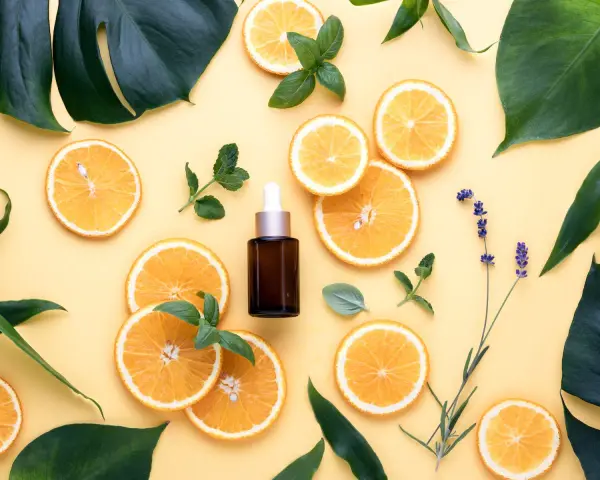 Siero viso con niacinamide e acido glicolico, circondato da fette d'arancia, foglie verdi e lavanda.