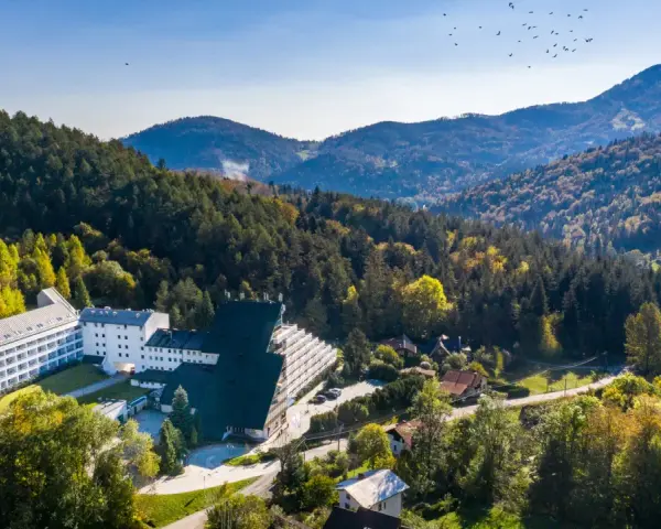 Malowniczy hotel przy stoku narciarskim w Polsce, otoczony jesiennym lasem. W oddali góry i niebo z ptakami.