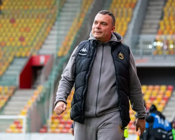 Mężczyzna w kamizelce Jagiellonii, być może omawia nowe jagiellonia transfery na tle pustych trybun stadionu.