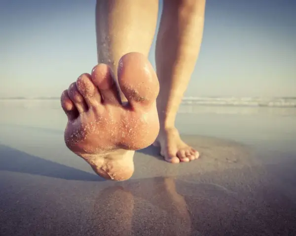 Paluch biegacza pokryty piaskiem, stopy na mokrym piasku przy plaży.