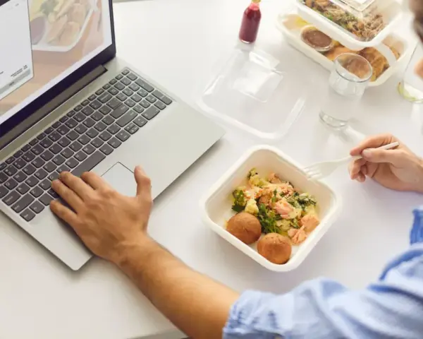 Mężczyzna je dietetyczny lunch z pudełka, pracując na laptopie.