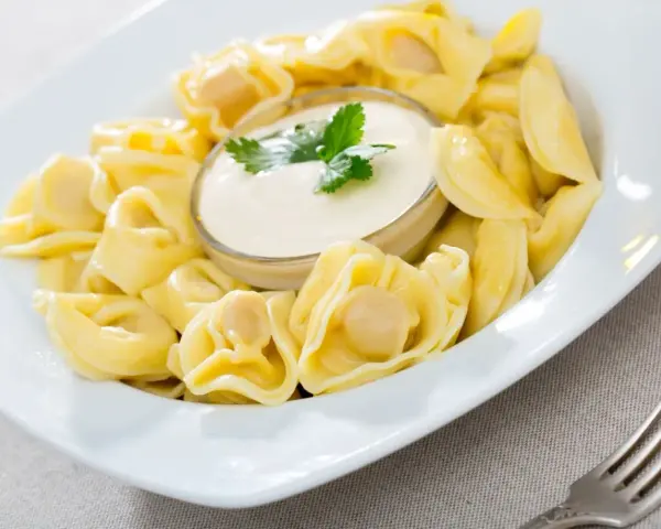 Pyszne pierożki tortellini w sosie śmietanowym, udekorowane natką pietruszki. Idealne danie na szybki obiad.