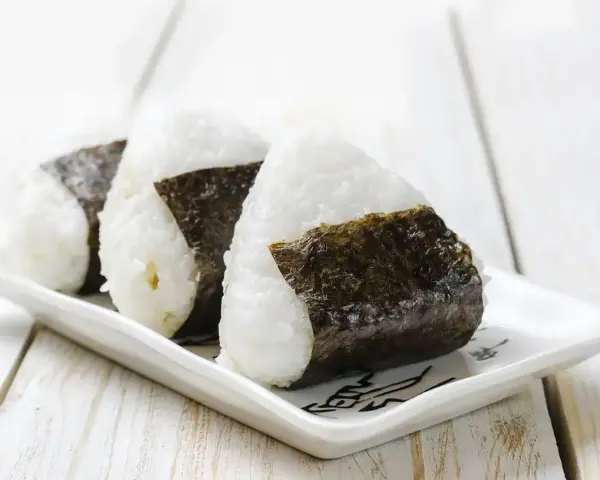 Trzy ryżowe kulki onigiri z nori na białym talerzyku. Idealne na szybki lunch, gdy szukasz prostego onigiri przepis.