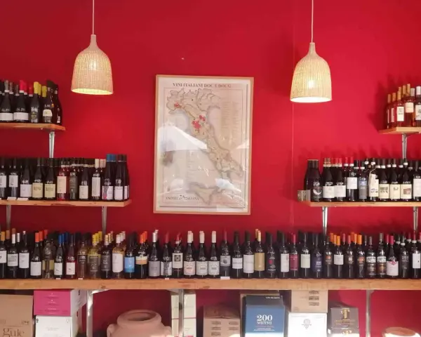 Regal voller italienischer Weinsorten vor roter Wand. Eine Karte Italiens mit Weinregionen hängt zentral.