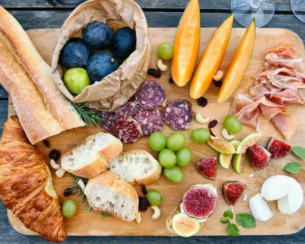 Tabla de quesos y embutidos: baguettes, croissants, higos, uvas, melón, jamón serrano y salami. Un festín que muestra qué comen los franceses.