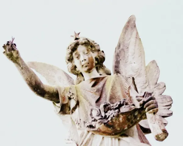 Kamienna figura anioła z gwiazdą na głowie, trzymająca w dłoniach kwiaty i gałązkę. Symbolika 2244 znaczenie.