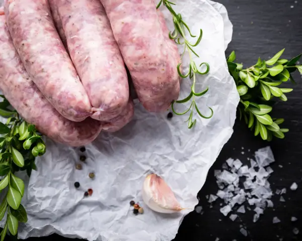 Surowa biała kiełbasa na papierze, obok gałązki rozmarynu i czosnek. Zastanawiasz się nad biała kiełbasa kcal?