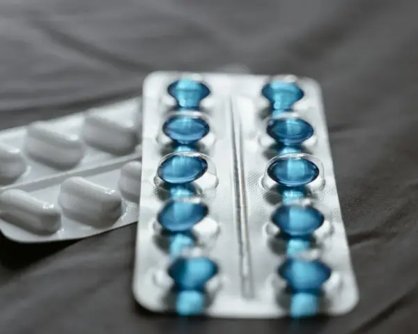 Dwa blistry leków: jeden z białymi kapsułkami, drugi z niebieskimi, które mogą być pregabalin sandoz.