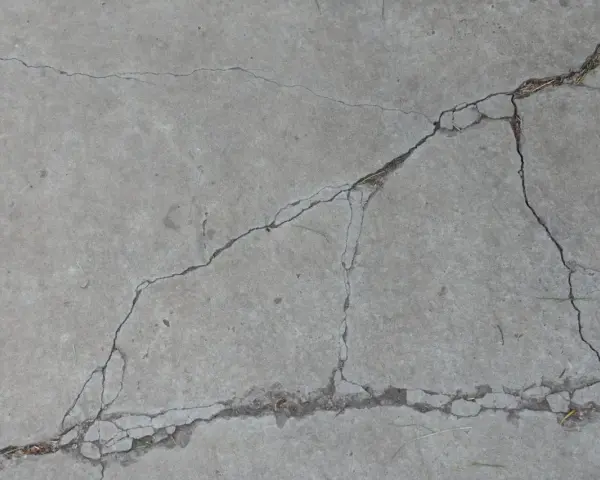 Popękany beton, jakby po długim okresie podlewania, z widocznymi szczelinami i drobnymi źdźbłami trawy.